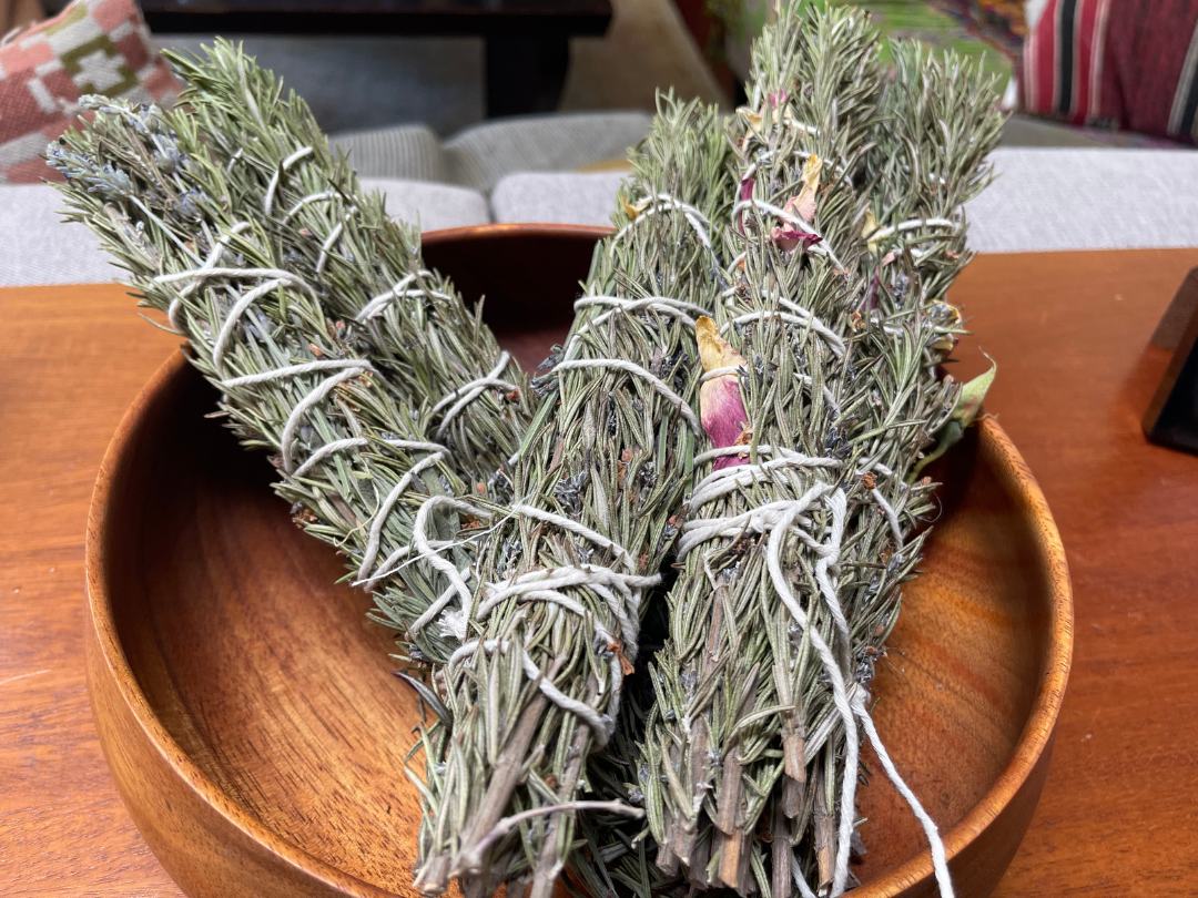four homemade rosemary smudge sticks on round wooden tray