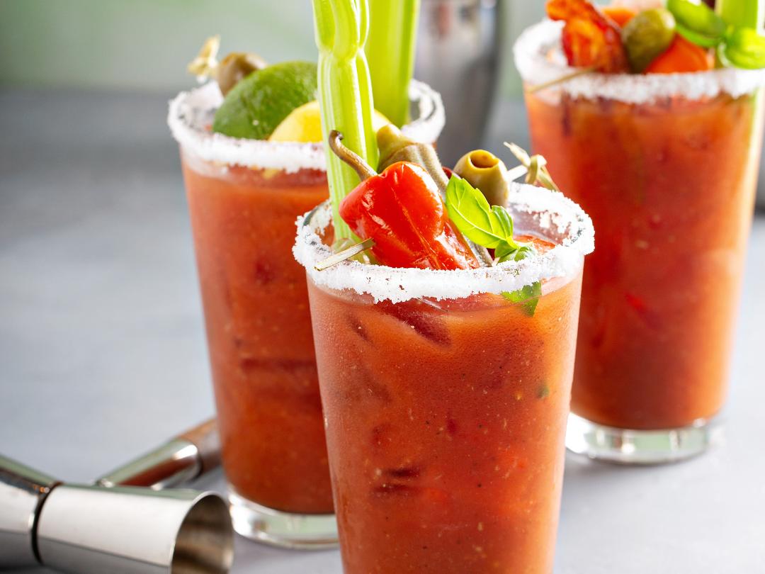 three bloody marys garnished with basil, chili pepper and celery stalks.