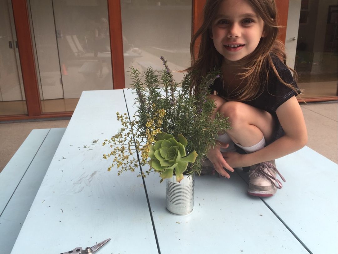 young girl sitting on picnic table next to a hand-picked bouquet of aeonium, rosemary, lavender, and the flower of a euphorbia.