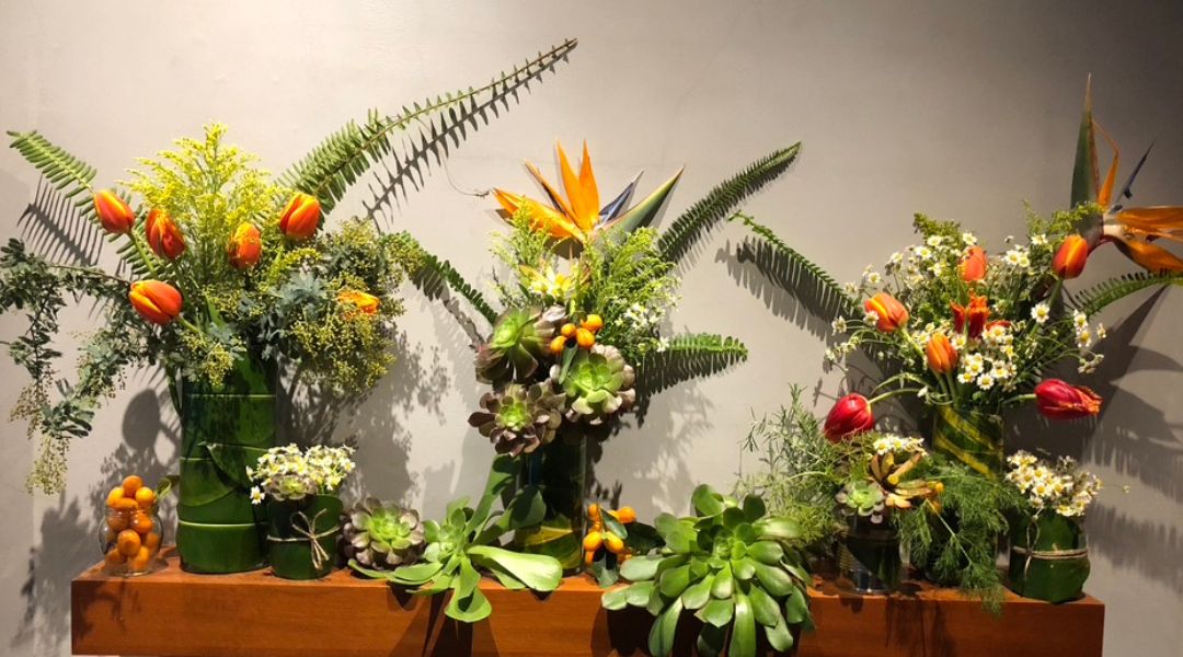 A stunning, colorful display of multiple floral arrangements using variety of aeonium mixed with tulips, ferns, chamomile, eucalyptus, kumquats, solidago, canna leaves, bird of paradise, and leucadendron. 