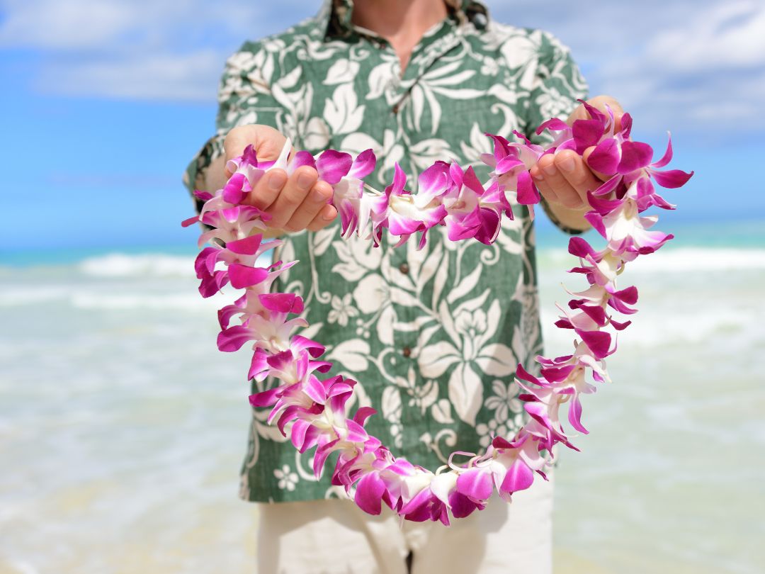 Man in Hawaiian shirt at beach holding a lei made of orchids