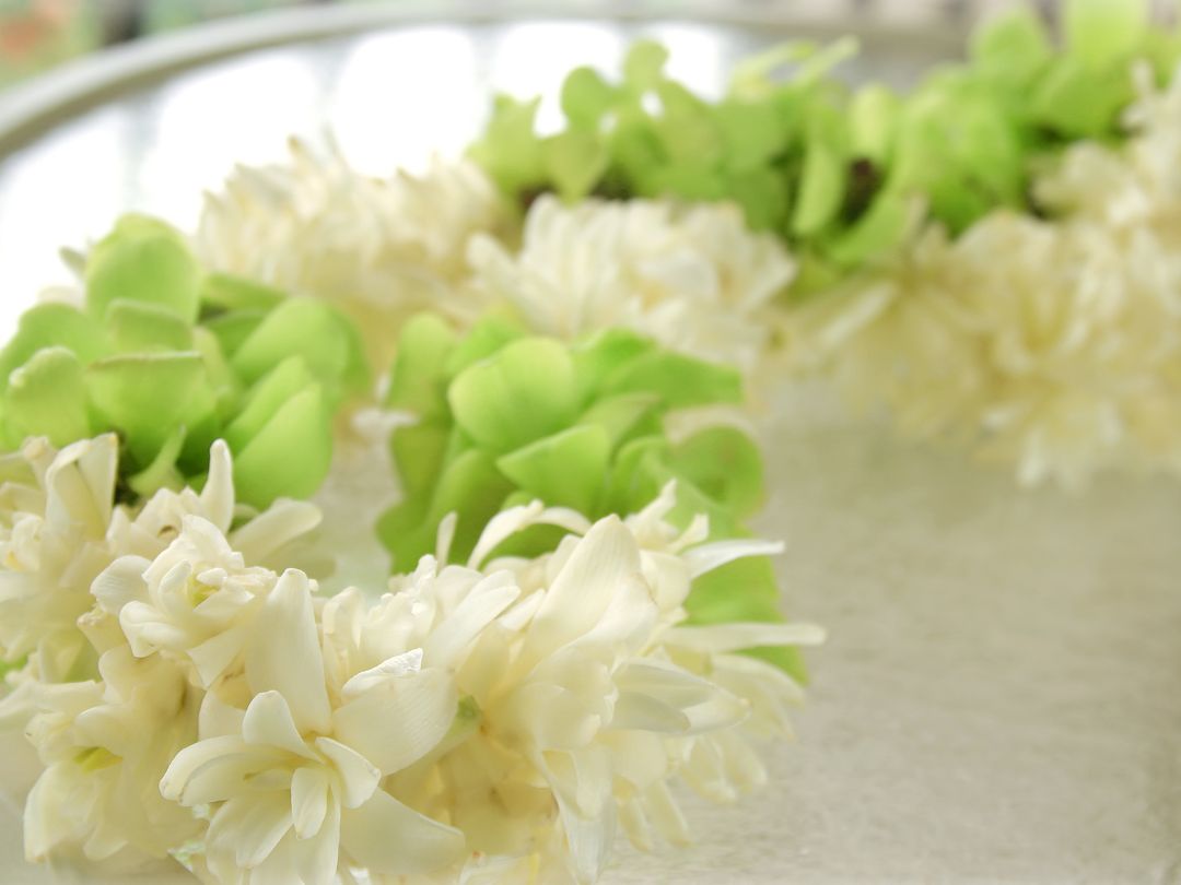 a lei made of white tuberose flower and green leaves on top of a glass table